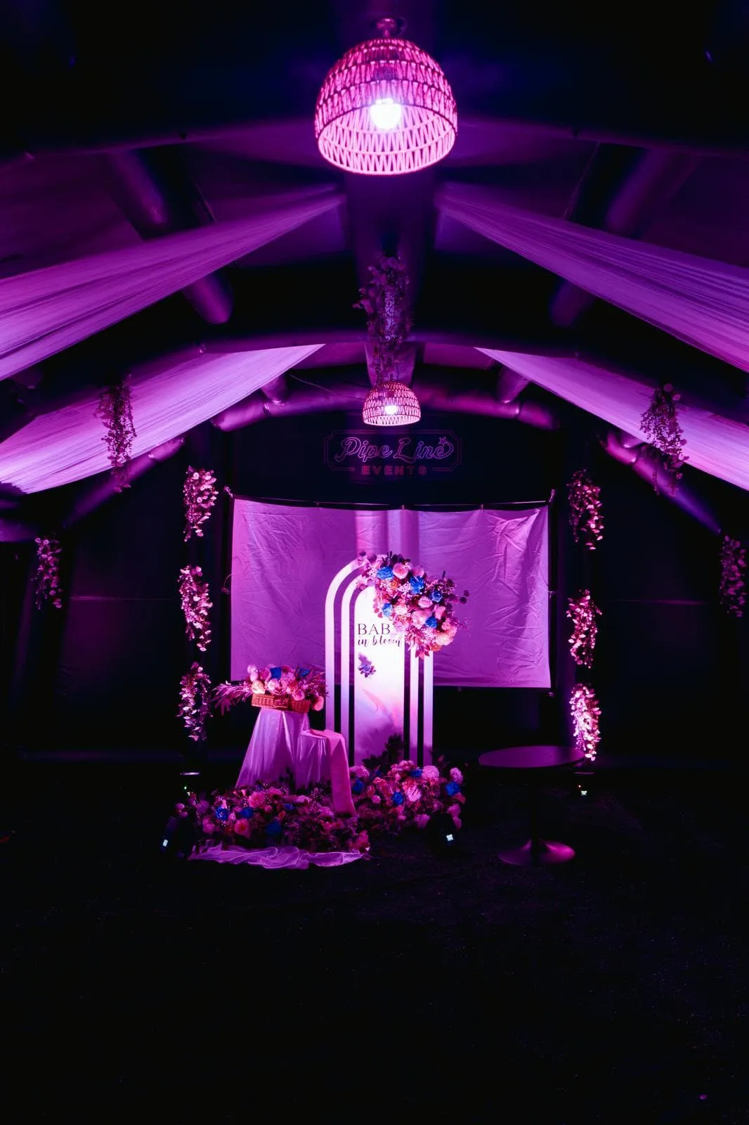 Baby in bloom baby shower setup with floral arch under pink lighting