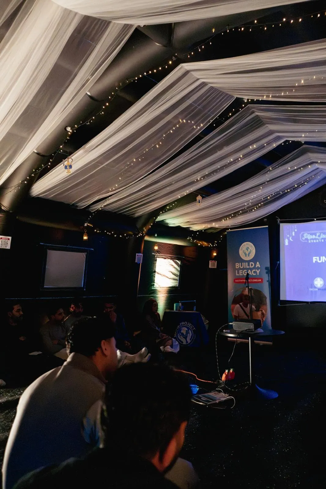 Charity event inside the Suite with white ceiling draping, fairy lights and a projector screen